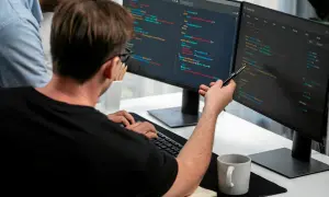 Dwóch programistów analizuje kod na monitorach. To świetny przykład, jak wygląda praca w IT dla początkujących – nauka i współpraca.