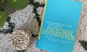 Boek "Patronen doorbreken" op een zachte, getextureerde ondergrond. Een plantje en een mandje liggen ernaast.