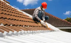 Trabajador aplica sellador para impermeabilizar un tejado de tejas y metal.