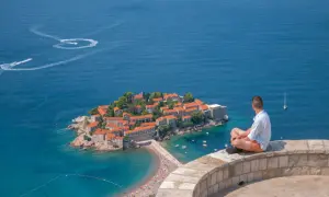 Czarnogóra na co uważać? Widok na wyspę Sveti Stefan, turysta kontempluje morze. Uważaj na słońce i tłumy na plaży.