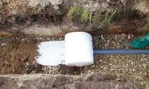 Budowa drenażu opaskowego wokół fundamentów. Rura drenarska owinięta geowłókniną, zasypana żwirem.