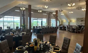 Elegancka sala bankietowa w ośrodku jeździeckim Lando, przygotowana na przyjęcie. Stoły nakryte czarnymi obrusami, złote talerze i eleganckie krzesła.