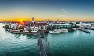 Friedrichshafen heute: Sonnenuntergang über dem Bodensee, mit Schiffen im Hafen und der Promenade.