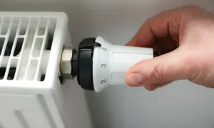 Dłoń reguluje termostat białego grzejnika elektrycznego panelowego, ustawiając temperaturę na 3.