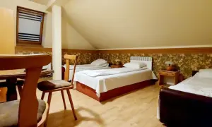 Pokój z trzema łóżkami, stolikami nocnymi i lampkami. W tle okno z żaluzjami. Wygodnie jak w domu w Korczowej.
