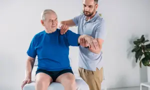 Fisioterapista assiste un anziano con debolezza muscolare, valutando la mobilità del braccio.