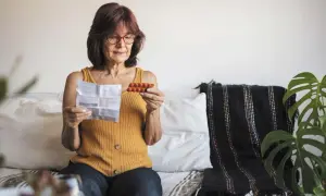 Kobieta czyta ulotkę leku, trzymając opakowanie tabletek. Szuka informacji o lekach na menopauzę bez recepty.
