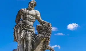 Statue de marbre d'Hercule, dieu grec, luttant contre un lion, sous un ciel bleu éclatant.