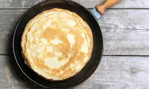 Ein Stapel goldbrauner, veganer Pfannkuchen liegt in einer Pfanne auf rustikalem Holz.