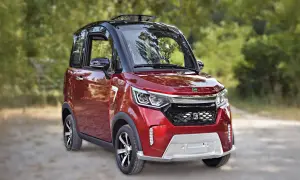 Auto rossa compatta, ideale per la mobilità ridotta, con tetto apribile e dettagli moderni, parcheggiata su una strada sterrata tra gli alberi.
