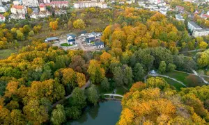 Jesienny widok na park Oruński w Gdańsku. Złote liście drzew otaczają staw, a w oddali widać zabudowania.