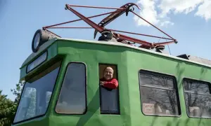 Uśmiechnięty mężczyzna w czerwonym swetrze wygląda z okna zielonej lokomotywy. To historyczna łódź Skierniewice, gotowa do podróży.