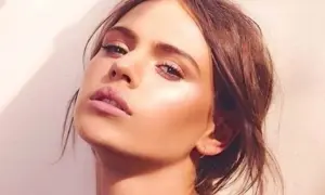 Visage d'une jeune femme au maquillage lumineux, elle pose avec un regard intense. Peut on bronzer avec du maquillage ? Sa peau semble éclatante.