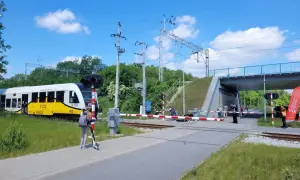 Pociąg KD zbliża się do przejazdu kolejowego. Dziewczynka na hulajnodze czeka na sygnał, by móc kontynuować wicie dojazd PKP.