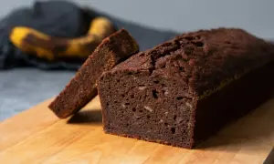 En saftig banankaka med choklad, en skiva är uppskuren. I bakgrunden syns en övermogen banan.
