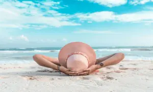 Osoba w kapeluszu leży na plaży, ręce za głową. To idealny przykład, co to znaczy last minute – spontaniczny relaks nad morzem.