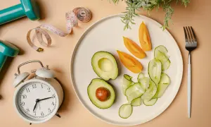 Zegar, miarka i talerz z awokado, pomidorami i ogórkiem – wszystko to symbolizuje dietę imitującą post i zdrowy styl życia.