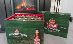 Dwie zielone skrzynki piwa Tyskie Niepasteryzowane Chmielone na zimno stoją obok siebie. W jednej widać rzędy butelek.