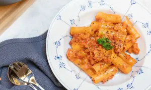 En tallrik med krämig pasta alla zozzona, toppad med persilja och svartpeppar. Bredvid ligger en servett och bestick.