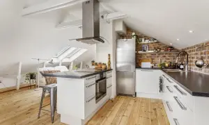 Accogliente cucina in mansarda bassa con soffitto spiovente, elettrodomestici in acciaio e mattoni a vista.