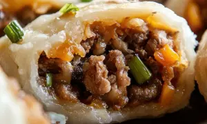 Pyszne pierogi z mięsem, z widocznym farszem i zieloną cebulką, kuszą apetycznym wyglądem.