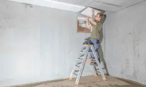 Mann montiert weiße Platten an der Kellerdecke zur Isolierung.