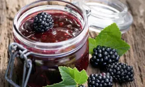 Glas mit Brombeermarmelade, daneben frische Brombeeren und Blätter. Perfekt, um sie mit Joghurt oder auf Toast zu mischen.