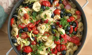 Kolorowa sałatka z tortellini, pomidorkami koktajlowymi, czarnymi oliwkami, papryką i natką pietruszki w patelni.