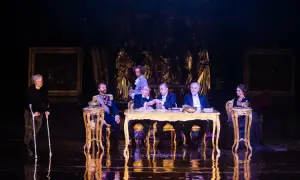 Scena z "Dziadów" w warszawskim teatrze. Przy złotym stole siedzą mężczyźni w strojach z epoki, obok kobieta na wózku.