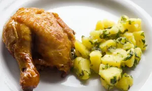 Pieczone udko kurczaka z ziemniakami i natką pietruszki na białym talerzu.