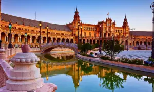 Plaza de España en Sevilla, una de las ciudades que ver en España. Reflejos dorados en el canal y un puente ornamentado.