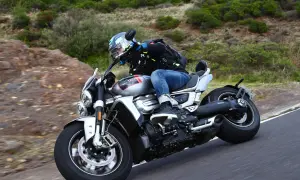 Motocyklista w kasku i kurtce jedzie na motocyklu Triumph Rocket 2 po krętej drodze wśród zieleni.