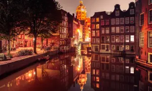 Amsterdam nocą, kanał z odbiciem zabytkowych kamienic i kościoła. Czerwona ulica Amsterdamu rozświetlona latarniami.