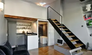 Interno moderno con cucina a vista, bagno piastrellato e scala a giorno. Le case con soffitti alti sfruttano lo spazio verticale con un soppalco visibile.