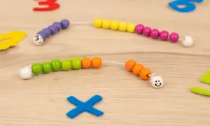 Bunte Perlenketten zum **rechenkette basteln** liegen auf Holz. Zahlen und ein blaues Kreuz sind im Hintergrund.
