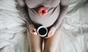 Gravid kvinna med en donut på magen och en kopp kaffe. Tänk på koffein gravid.