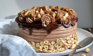Torta di buon compleanno al cioccolato e nocciole, con glassa lucida e decorazioni golose.