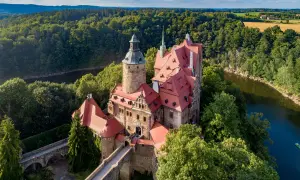 Zamek Czocha, malowniczo położony nad rzeką, otoczony bujną zielenią.