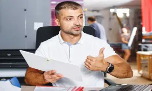 Mężczyzna w białej koszulce trzyma dokument i pokazuje kciuk w górę.