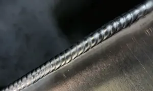 Precyzyjne spawanie aluminium migomatem. Widoczny gładki, lśniący ścieg spawalniczy na metalowej powierzchni.