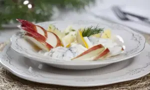 Pyszne śledzie w śmietanie z jabłkiem i koperkiem, podane na eleganckim talerzu, idealne na świąteczny stół.