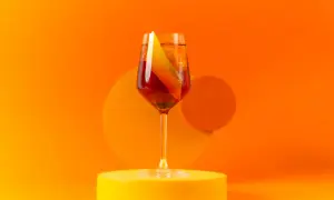 Ein Glas Aperitif mit Orangenscheibe auf gelber Unterlage vor orangefarbenem Hintergrund.