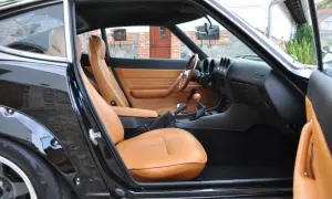 Wnętrze klasycznego Datsuna 280Z z brązową skórzaną tapicerką i drewnianą kierownicą.