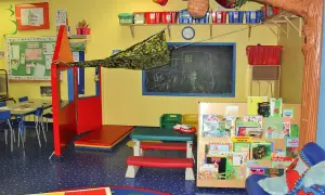 Ein farbenfroher Gruppenraum mit Spielzeug, Büchern und einer Tafel, der den Raum als dritten Erzieher für Kinder gestaltet.
