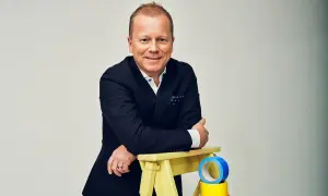 Claes Seldeby, en glad man i kostym, lutar sig mot en gul pall med blå och gul tejp.