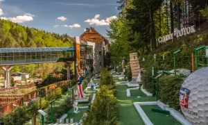 Mini golf z atrakcjami jak Krzywa Wieża w Pizie i Statua Wolności, na tle lasu i budynku.