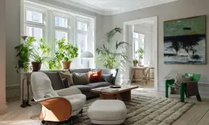 Ett vardagsrum med bohemisk inredning, fyllt med gröna växter, en bekväm soffa och en konstnärlig tavla på väggen.