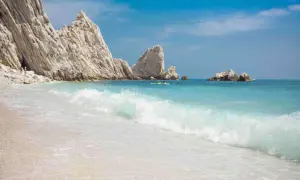 Spiaggia delle Due Sorelle: onde turchesi lambiscono la riva, rocce bianche imponenti si ergono sul mare azzurro, un paradiso incontaminato.