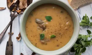 Aksamitna zupa grzybowa z suszonych grzybów, doprawiona świeżo mielonym pieprzem i ozdobiona listkami oregano. Obok leżą suszone grzyby i kromka chleba.