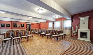 Elegancka sala konferencyjna w Lanckorona Hotel Modrzewiówka, z rzędami krzeseł, portretami na ścianach i ozdobnym piecem.